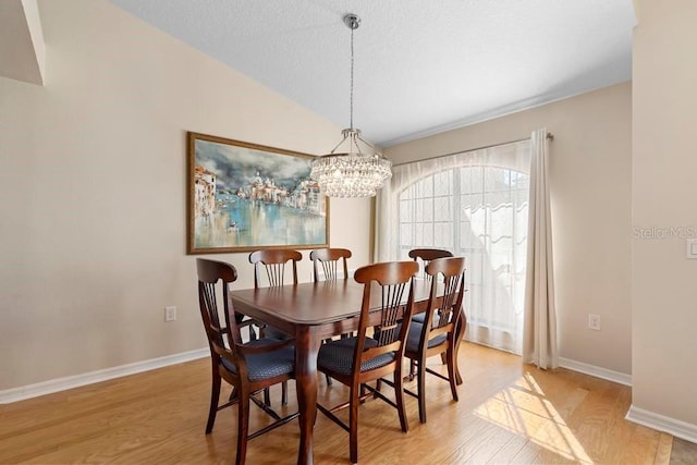 dining area featuring light wood finished floors, a notable chandelier, baseboards, and vaulted ceiling