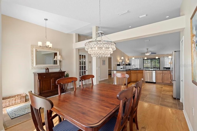 dining area featuring baseboards, ceiling fan with notable chandelier, light wood-style flooring, and vaulted ceiling