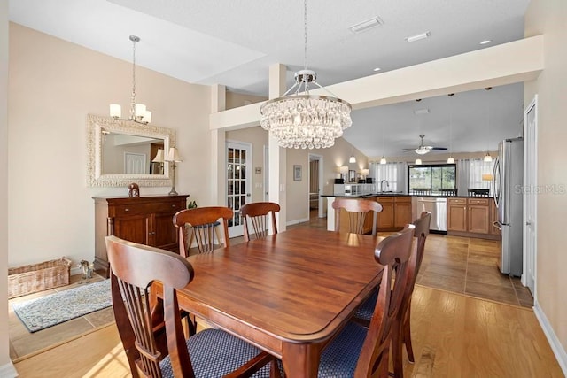 dining area featuring baseboards, ceiling fan with notable chandelier, light wood-style flooring, and vaulted ceiling