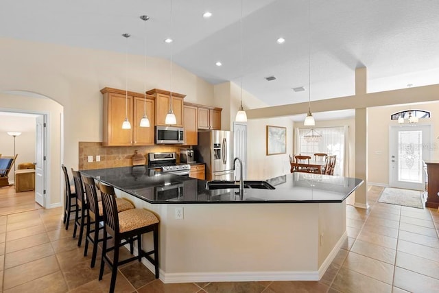 kitchen with a sink, arched walkways, appliances with stainless steel finishes, decorative backsplash, and lofted ceiling