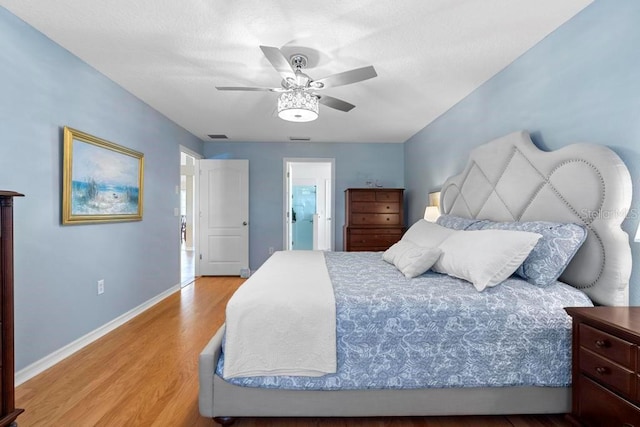 bedroom featuring wood finished floors, visible vents, baseboards, ceiling fan, and connected bathroom