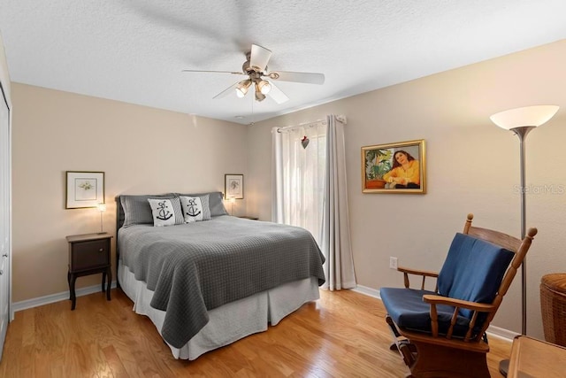 bedroom featuring light wood-style flooring, a textured ceiling, a ceiling fan, and baseboards