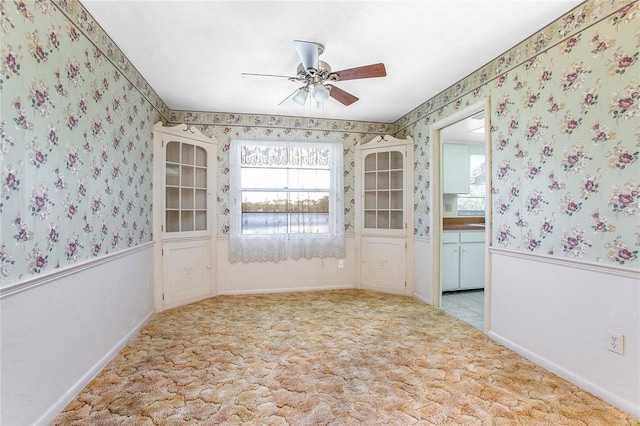 empty room with light carpet, a ceiling fan, wainscoting, and wallpapered walls