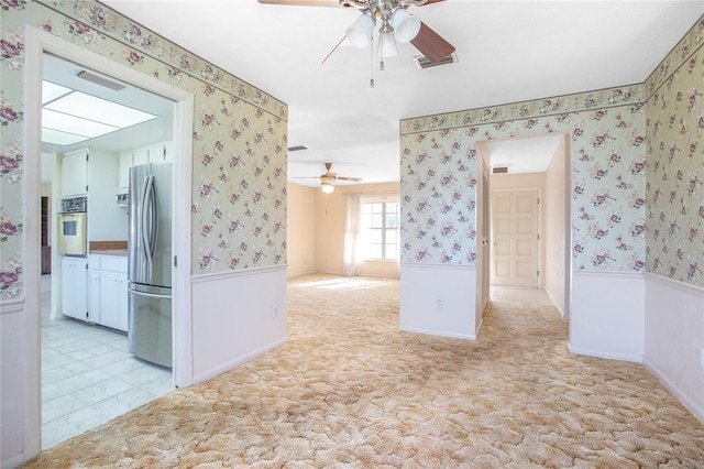 unfurnished room featuring wallpapered walls, light colored carpet, visible vents, and wainscoting