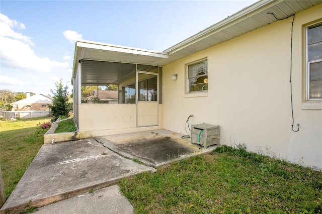 view of side of property featuring stucco siding, a lawn, and a sunroom