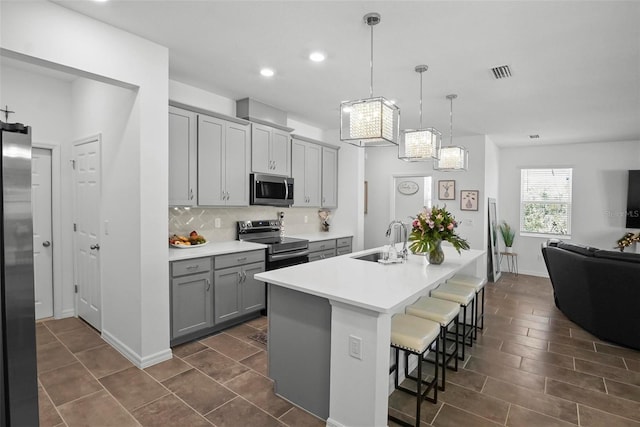 kitchen featuring visible vents, a sink, decorative backsplash, gray cabinetry, and stainless steel appliances