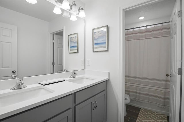 full bath featuring double vanity, toilet, an inviting chandelier, and a sink