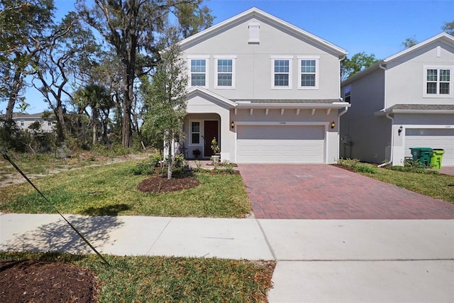 traditional-style house featuring decorative driveway, an attached garage, and stucco siding