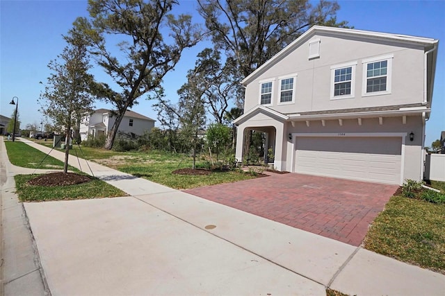 traditional-style house with a front lawn, decorative driveway, an attached garage, and stucco siding