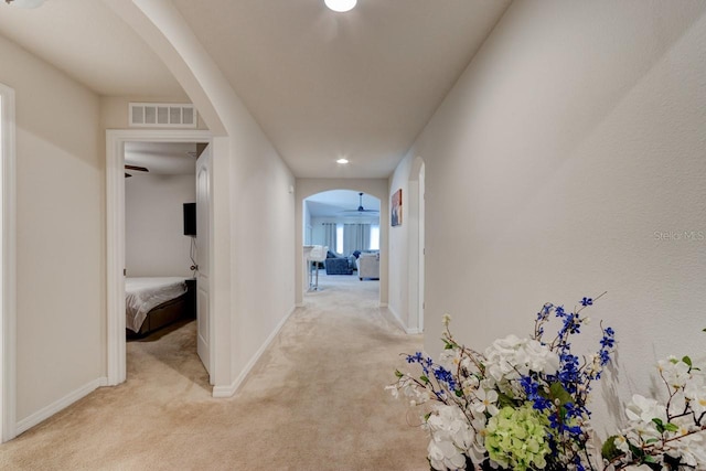 corridor with baseboards, visible vents, arched walkways, and light carpet