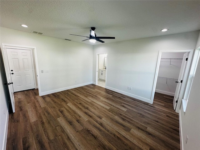 unfurnished bedroom with visible vents, a walk in closet, dark wood-type flooring, baseboards, and a textured ceiling