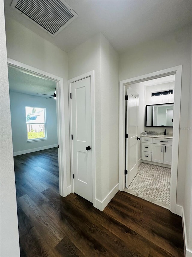 hall with visible vents, baseboards, and dark wood finished floors