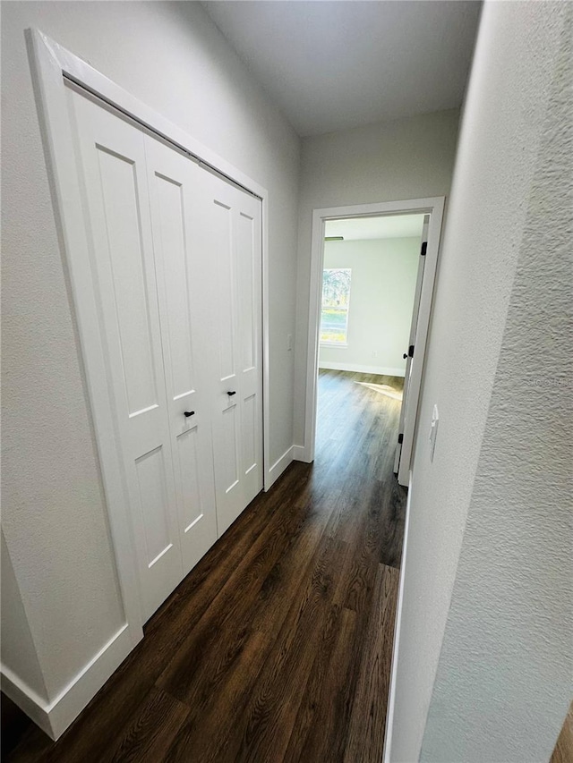 hall with dark wood-style floors, baseboards, and a textured wall