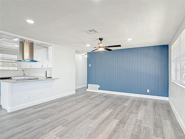 unfurnished living room with a wealth of natural light, visible vents, light wood-style flooring, and a ceiling fan