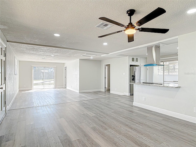 unfurnished living room with visible vents, baseboards, light wood-type flooring, a textured ceiling, and a ceiling fan