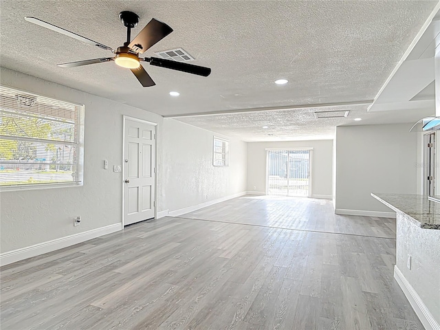 unfurnished living room with baseboards, visible vents, light wood-style flooring, a textured ceiling, and a textured wall