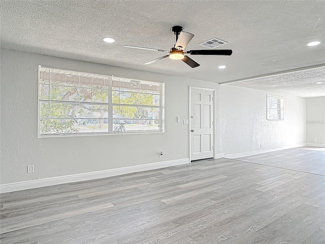 unfurnished living room featuring visible vents, baseboards, wood finished floors, a textured ceiling, and a ceiling fan