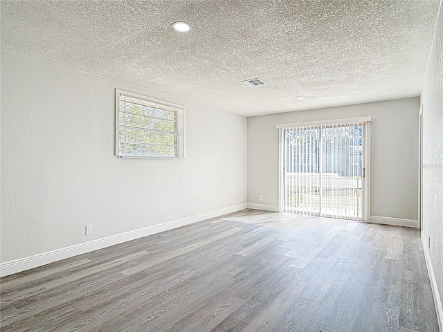 empty room with visible vents, plenty of natural light, baseboards, and wood finished floors