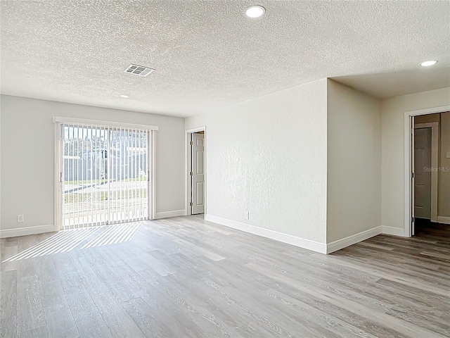 empty room featuring visible vents, baseboards, a textured ceiling, and wood finished floors