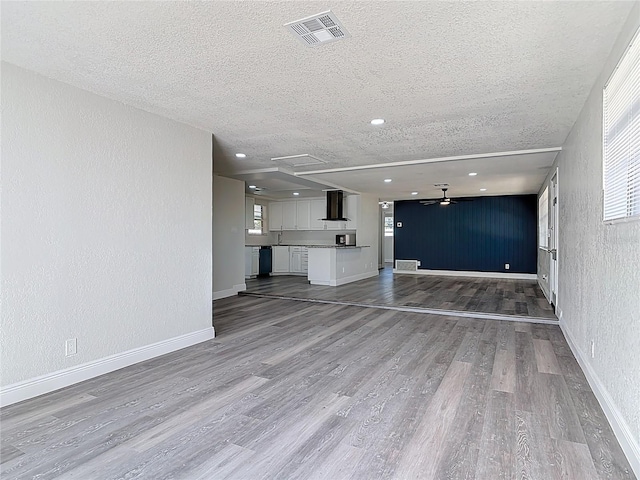 unfurnished living room featuring visible vents, a textured ceiling, wood finished floors, ceiling fan, and a textured wall