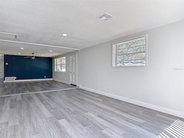 unfurnished room featuring visible vents, a textured ceiling, wood finished floors, baseboards, and ceiling fan