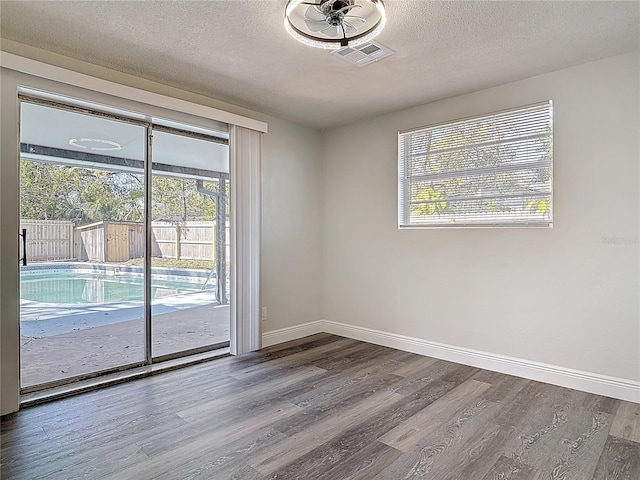 unfurnished room featuring visible vents, baseboards, a textured ceiling, and wood finished floors