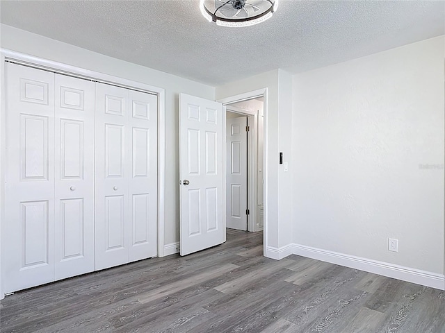 unfurnished bedroom featuring a closet, a textured ceiling, baseboards, and wood finished floors