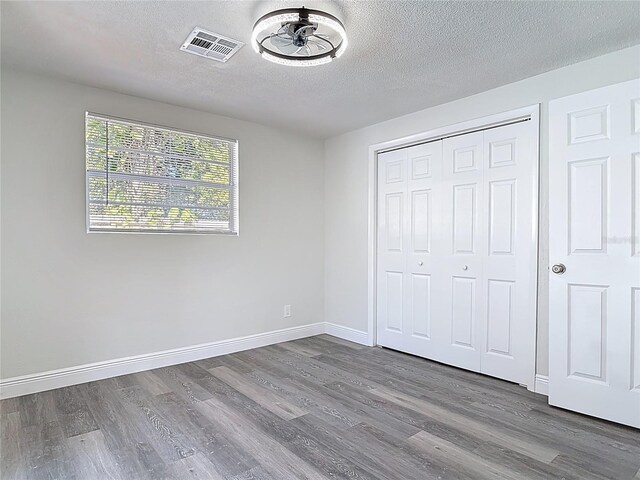 unfurnished bedroom featuring visible vents, a textured ceiling, wood finished floors, a closet, and baseboards