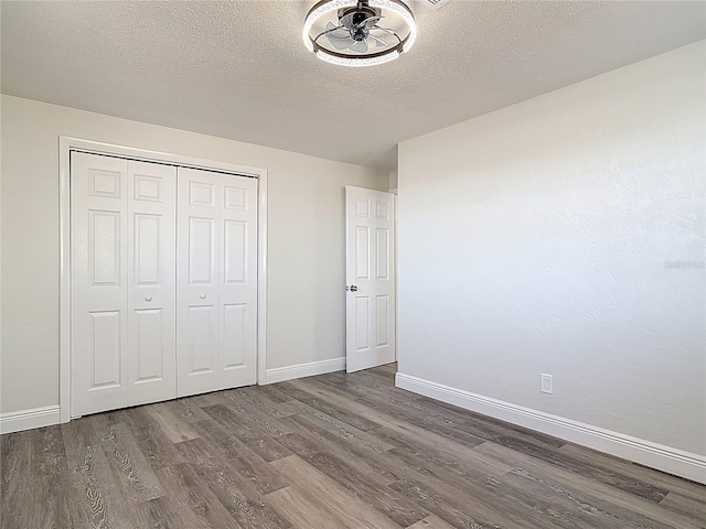 unfurnished bedroom featuring a closet, baseboards, a textured ceiling, and wood finished floors