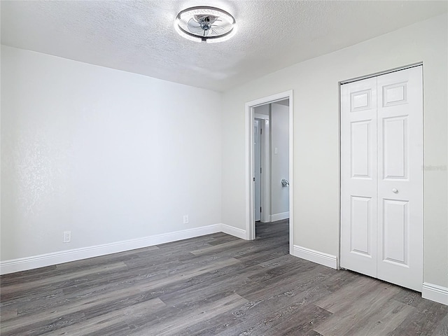 unfurnished bedroom featuring a closet, baseboards, a textured ceiling, and dark wood-style floors