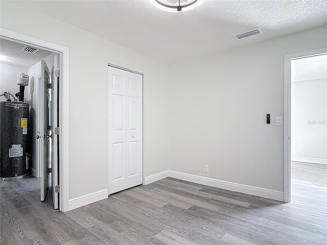 unfurnished bedroom with visible vents, electric water heater, wood finished floors, and a textured ceiling