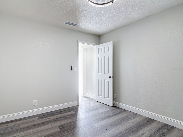 spare room featuring visible vents, a textured ceiling, baseboards, and wood finished floors