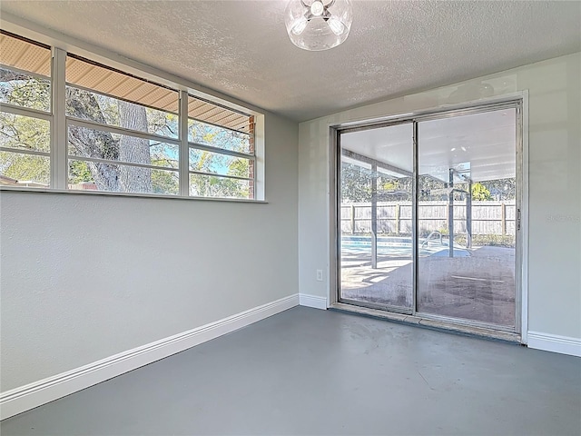 spare room with finished concrete floors, plenty of natural light, a textured ceiling, and baseboards