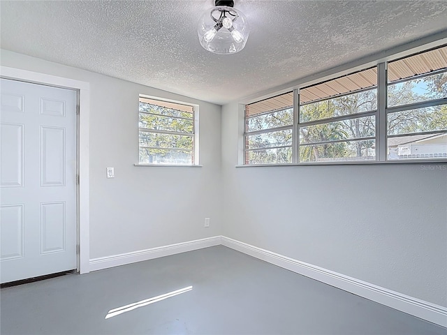 empty room with baseboards, a textured ceiling, and concrete flooring