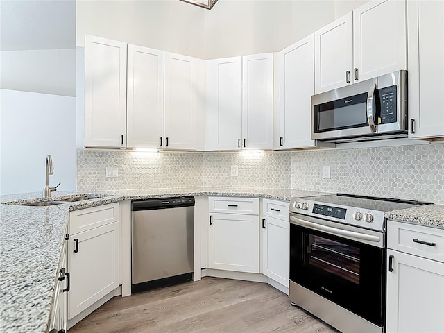 kitchen with light wood finished floors, tasteful backsplash, appliances with stainless steel finishes, white cabinetry, and a sink