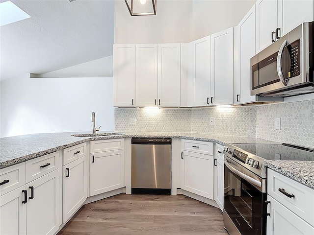 kitchen with backsplash, light wood-type flooring, appliances with stainless steel finishes, white cabinets, and a sink