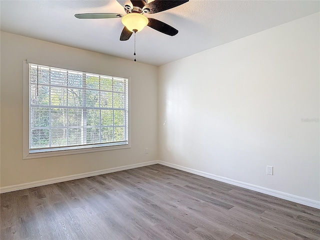 empty room with a healthy amount of sunlight, ceiling fan, baseboards, and wood finished floors