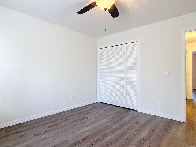 unfurnished bedroom featuring a ceiling fan, dark wood-style floors, baseboards, and a closet