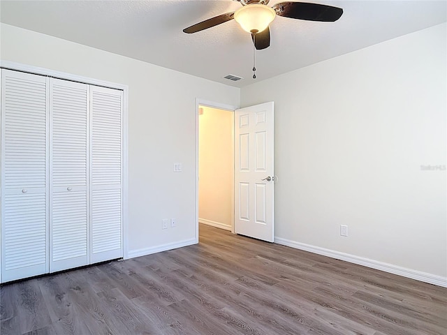 unfurnished bedroom with a closet, visible vents, baseboards, and wood finished floors