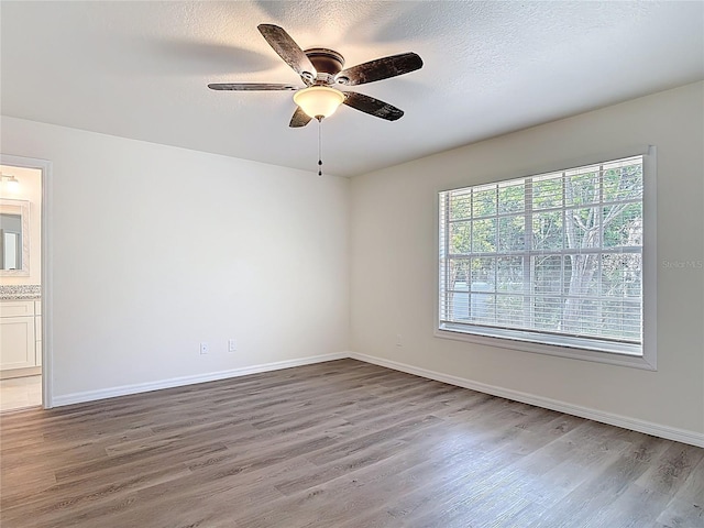 empty room with a ceiling fan, wood finished floors, baseboards, and a textured ceiling