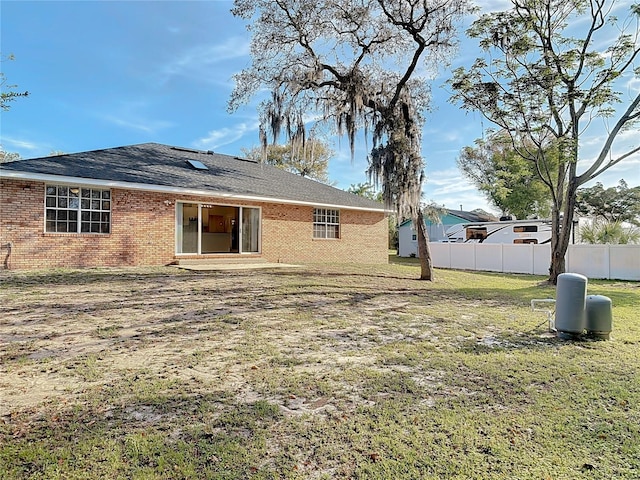 back of house with brick siding, a lawn, and fence