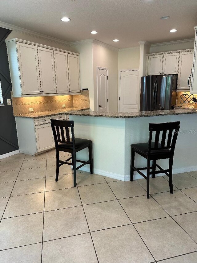 1812 Leather Fern Dr, Ocoee, FL 34761 - kitchen with freestanding refrigerator, ornamental molding, tasteful backsplash, a breakfast bar area, and dark stone counters