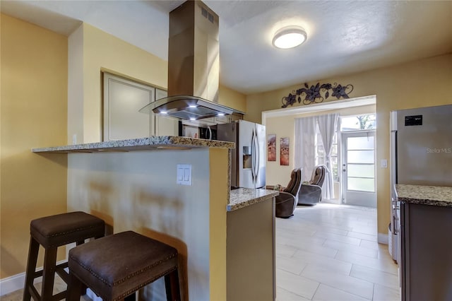 kitchen with baseboards, light stone countertops, a kitchen bar, stainless steel refrigerator with ice dispenser, and island range hood