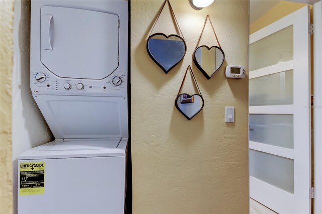 laundry area with laundry area, a textured wall, and stacked washer / drying machine