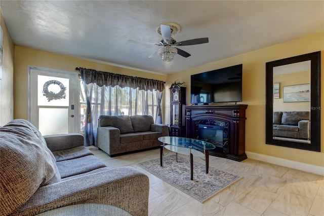 living room featuring a glass covered fireplace, baseboards, and ceiling fan