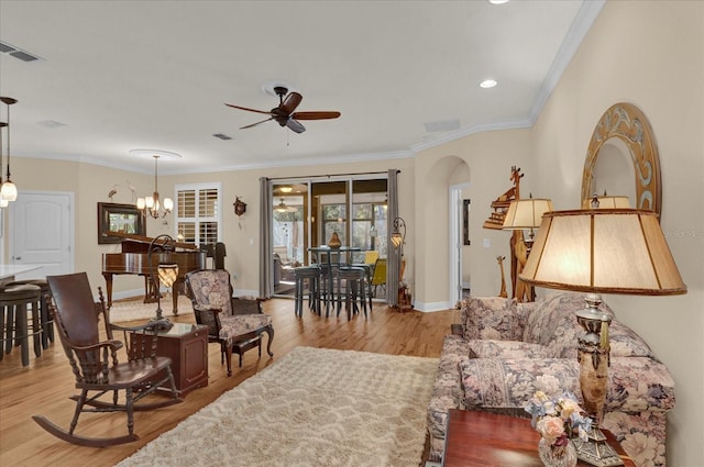 living room featuring visible vents, ornamental molding, ceiling fan with notable chandelier, wood finished floors, and arched walkways