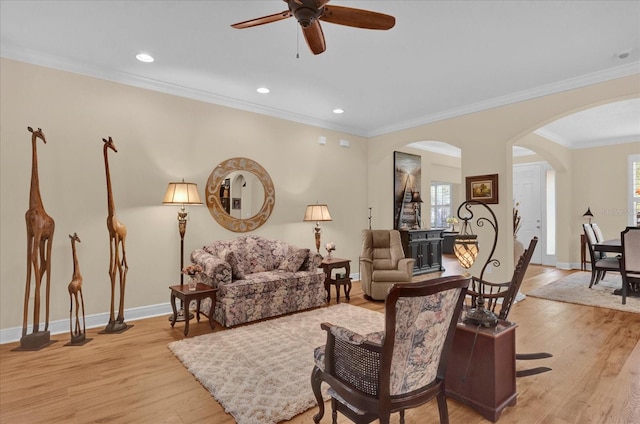 living area featuring light wood-style floors, a ceiling fan, arched walkways, and baseboards