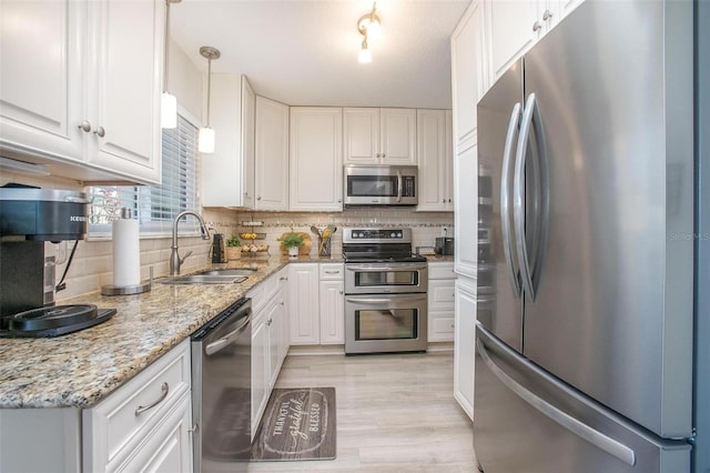 kitchen with tasteful backsplash, light stone countertops, white cabinets, stainless steel appliances, and a sink