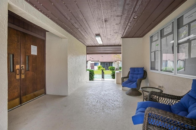 sitting room with concrete flooring, wooden ceiling, and a textured wall