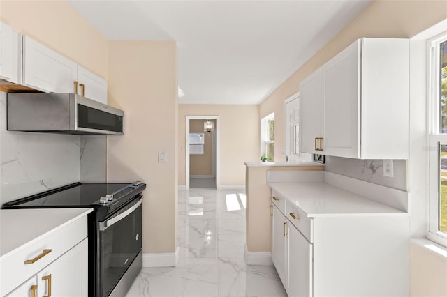 kitchen featuring marble finish floor, black range with electric stovetop, stainless steel microwave, white cabinetry, and light countertops